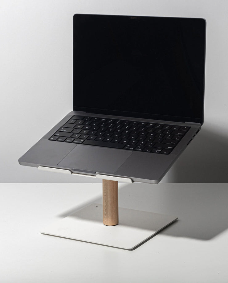 A black-screen laptop rests on the Gather Laptop Stand (White/Maple), featuring a maple rod and white base, placed on a white table against a plain light background.