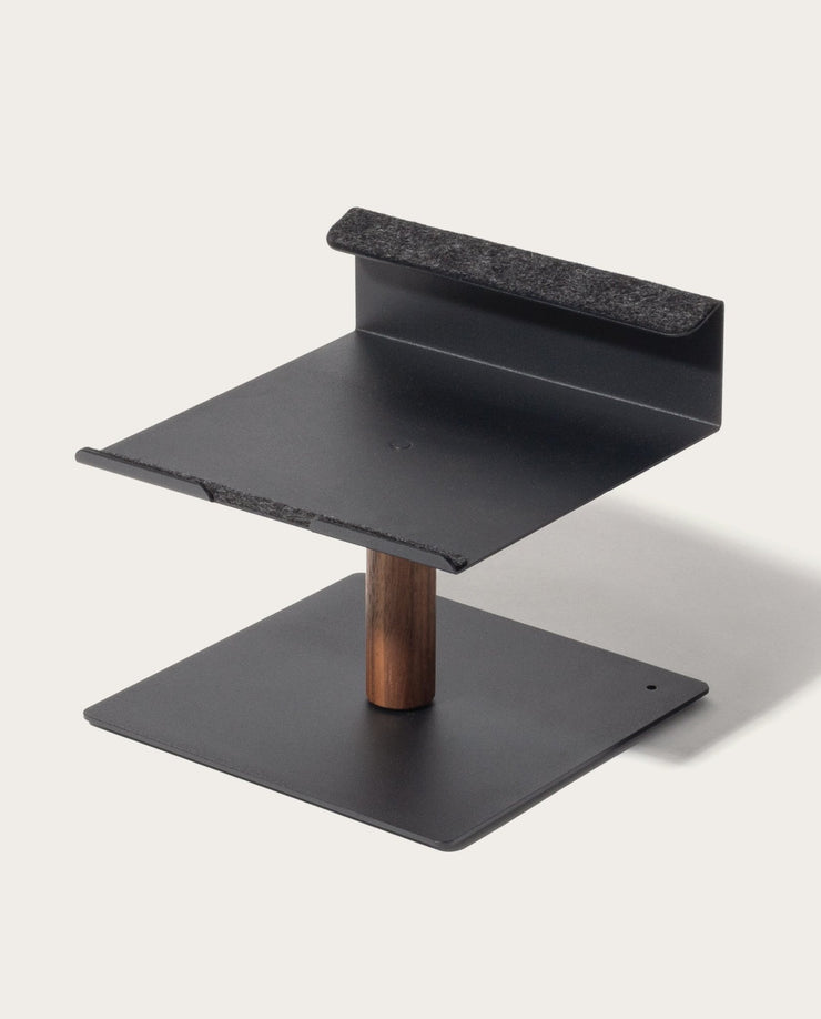 The Gather Laptop Stand (Black/Walnut) is a modern, minimalist ergonomic stand with a flat base, vertical walnut support, and raised platform with felt-lined edge for secure device holding—expertly made in the USA.