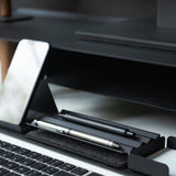 A smartphone, pens, and a stylus are neatly arranged in a black Gather Zigzag Tray (2x1) made from powder-coated steel beside a computer keyboard on a modern, minimal workspace.