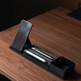 A wooden desk displays the Gather 1x4 Organizer Set (Black), holding a smartphone, white pen, gold pen, and an open compartment for storage, all in a sleek minimalist and modern style.