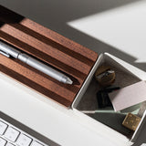 A close-up of a white desk with a keyboard, Gather Small Tray (1x1 - White) as a desk organizer holding a sharpener, eraser, SD card, paper clips, notepads, and wooden pen holder. Sunlight casts shadows across the items. Pen holder is made in Pennsylvania.
