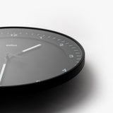 The Braun Wall Clock (Black) features minimalist white hour markers and hands, shown at an angle with only the lower right of the face visible against a white background. An easy-to-read clock, ideal for any modern space.