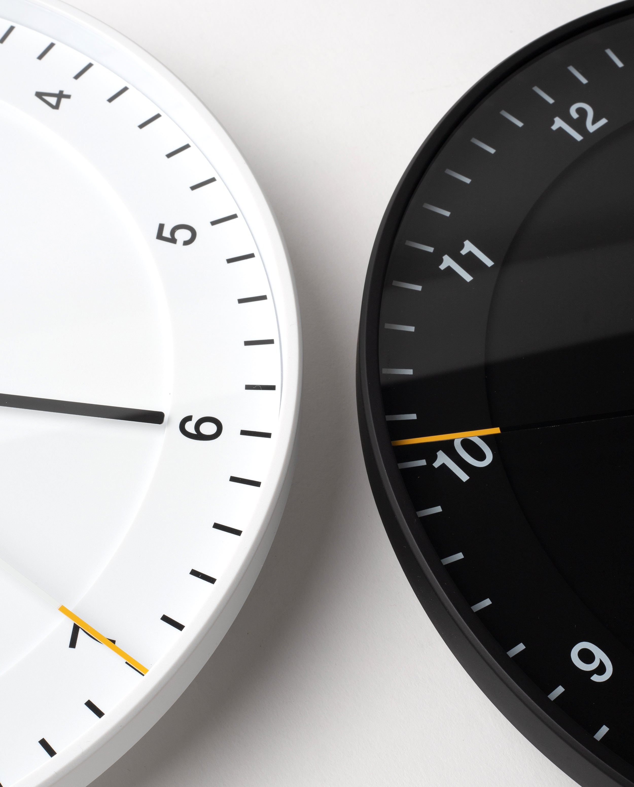 Two Braun Wall Clocks, one in white and one in black, are shown side by side, each featuring an easy-to-read dial and modern design. Both display the time as 6:50. The clocks are cropped to reveal only portions of their faces against a pale background, drawing attention to the Braun Wall Clock (White) and its silent sweeping second hand.