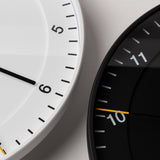Close-up of two modern wall clocks—a white easy-to-read clock showing numbers 4 to 6 and a black Braun Wall Clock, both with minimalist designs and styled for contemporary spaces.