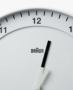 Close-up of a Braun Wall Clock (White), displaying the time as 12:04. The image focuses on the upper section of the clock face, which features bold black hour markers and black hands set against a white background. The design includes an easy-to-read dial and a silent sweeping second hand.