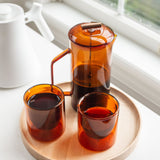 A handcrafted Round Valet Tray (Maple - Large), made in Pennsylvania, holds a transparent amber glass French press and two matching cups filled with dark coffee, placed on a white surface near a window.