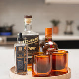 A selection of alcohol bottles and glasses is displayed on the Round Valet Tray (Maple - Large), a handcrafted piece made in Pennsylvania.