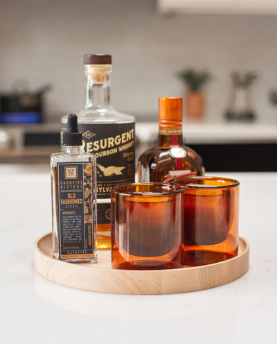 A selection of alcohol bottles and glasses is displayed on the Round Valet Tray (Maple - Large), a handcrafted piece made in Pennsylvania.