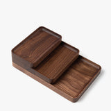 Three Valet Tray (Walnut - Small) pieces, handcrafted in Pennsylvania, are stacked on a white background. Their rounded edges highlight the walnut grain, providing a stylish solution for everyday carry storage.