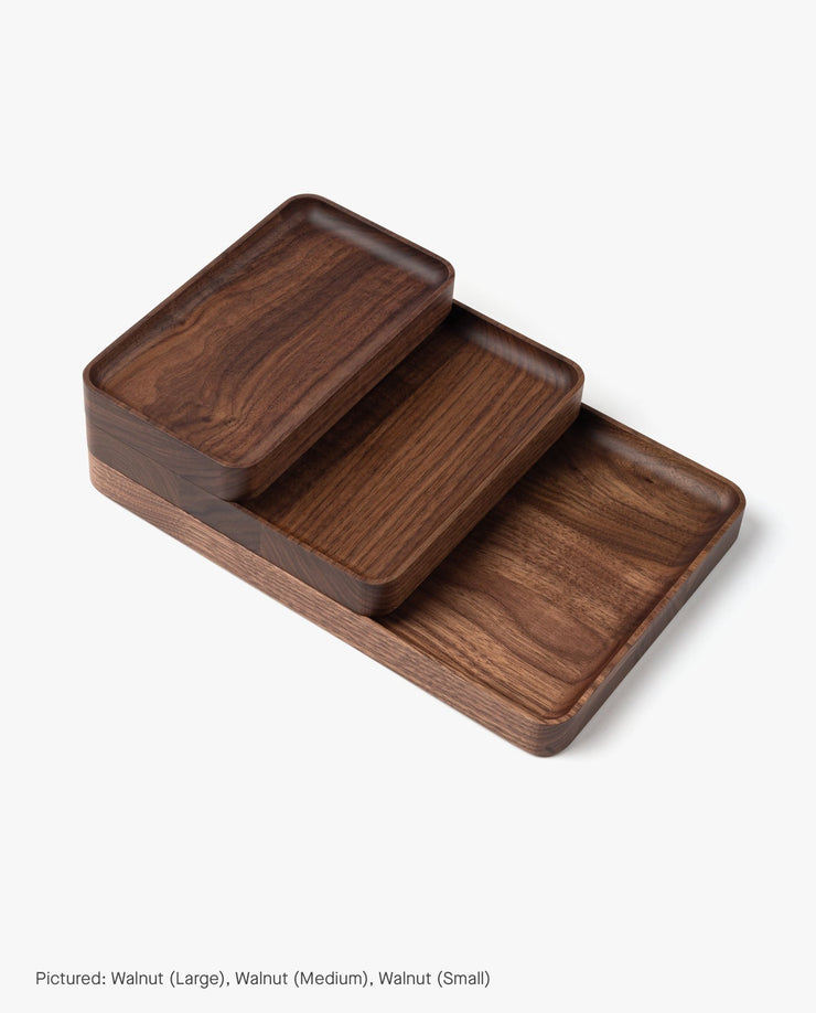 Three Valet Tray (Walnut - Small) pieces, handcrafted in Pennsylvania, are stacked on a white background. Their rounded edges highlight the walnut grain, providing a stylish solution for everyday carry storage.
