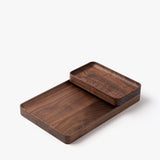 The Small Walnut Valet Tray, handcrafted in Pennsylvania, features rounded edges for elegant everyday carry storage, shown stacked partially atop a larger tray on a white background.