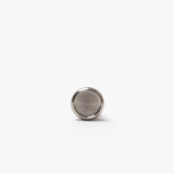 A small, round, silver-colored button battery rests on a white background, evoking the sleek closures featured on the Discbound Heirloom Journal Bundle (Black Leather - Standard 6" x 8.5" + 3 Refills).