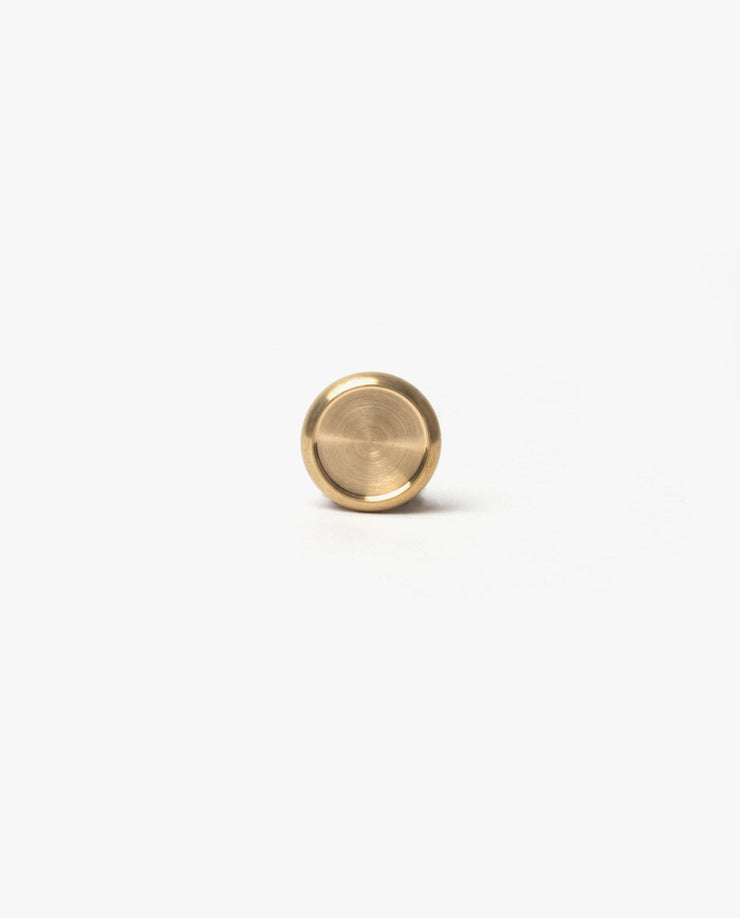A small, round brass disc with a raised rim, like those in the Discbound Heirloom Journal (Tan Leather - Standard 6" x 8.5"), is centered on a plain white background.