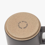 A close-up of an upside-down Hasami Porcelain Mug (Matte Black) shows its tan bottom stamped with "HASAMI PORCELAIN JAPAN," emphasizing its handmade quality. The mug’s handle is visible on the right side.