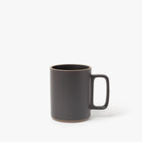 The Hasami Porcelain Mug (Matte Black) features a large rectangular handle and natural brown ceramic edges on the rim and base, highlighting its handmade look inspired by classic Japanese design. Photographed against a plain white background.