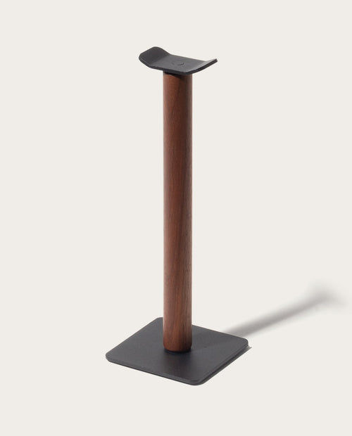 The Gather Headphone Stand (1x1 - Black/Walnut) features a solid walnut vertical column, a black powder coated steel base, and a curved top to hold headphones, all set against a plain light background.