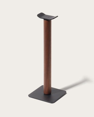 The Gather Headphone Stand (1x1 - Black/Walnut) features a solid walnut vertical column, a black powder coated steel base, and a curved top to hold headphones, all set against a plain light background.