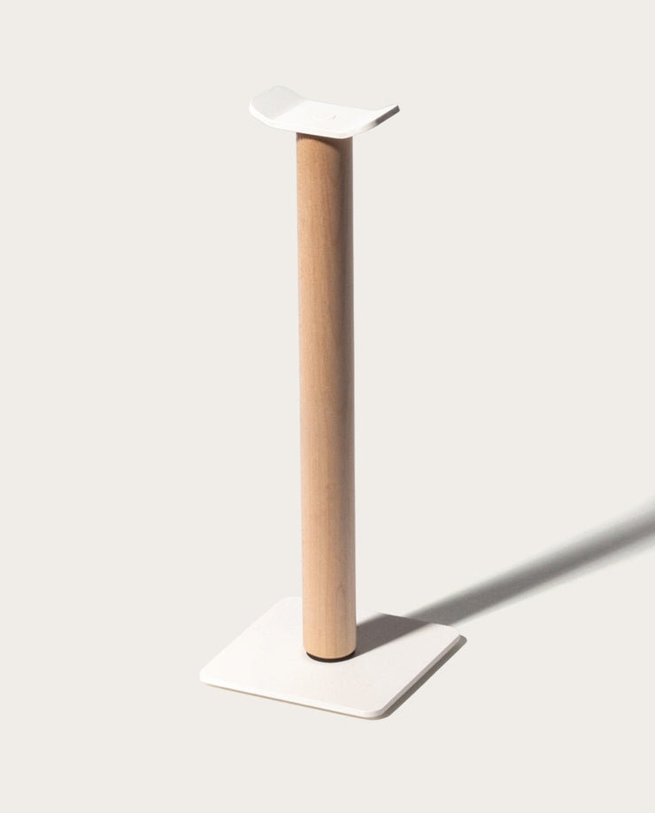 The Gather Headphone Stand (1x1 - White/Maple) features a tall maple wood post, a square white base, and a curved white top platform, all set against a simple light background for a minimalist look.