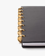 A close-up of the Discbound Heirloom Journal Bundle in black leather (Standard 6" x 8.5" + 3 refills), featuring large gold rings binding the left edge, shown against a plain white background.