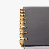 A close-up of the Discbound Heirloom Journal Bundle in black leather (Standard 6" x 8.5" + 3 refills), featuring large gold rings binding the left edge, shown against a plain white background.