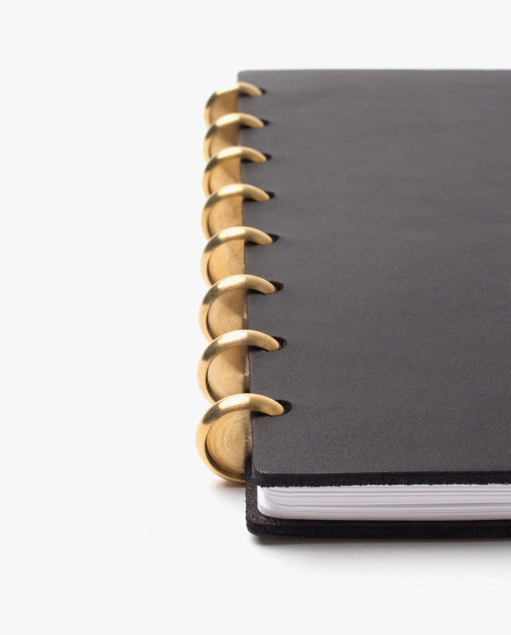 A close-up of the Discbound Heirloom Journal Bundle in black leather (Standard 6" x 8.5" + 3 refills), featuring large gold rings binding the left edge, shown against a plain white background.
