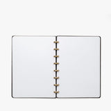 The Discbound Heirloom Journal Bundle (Black Leather - Standard 6" x 8.5" + 3 Refills) is open to blank white pages, showcasing its gold-colored ring binding, viewed from above on a white background.