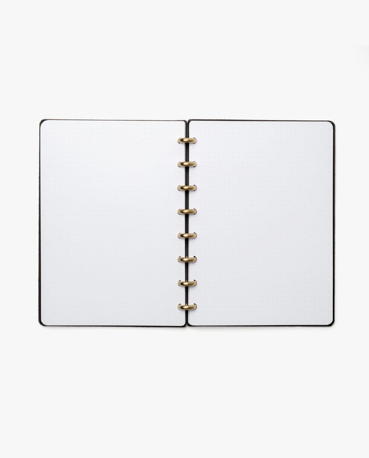The Discbound Heirloom Journal Bundle (Black Leather - Standard 6" x 8.5" + 3 Refills) is open to blank white pages, showcasing its gold-colored ring binding, viewed from above on a white background.