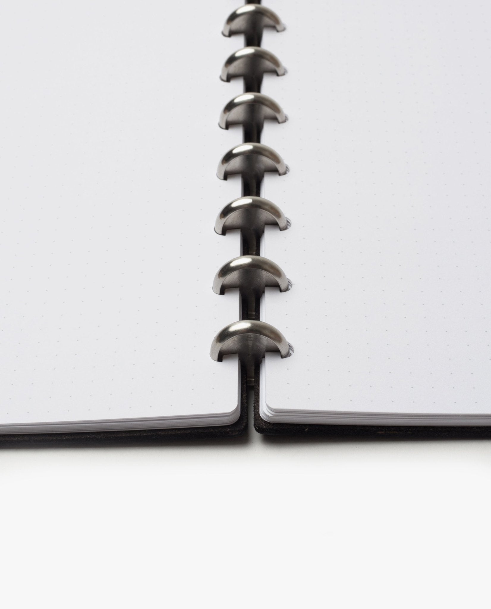 Close-up of the Discbound Heirloom Journal (Black Leather - Standard 6" x 8.5") showing dotted refillable pages and metal disc binding rings, viewed from the bottom center against a white background.