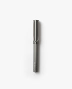 A LAMY Lx Rollerball (Ruthenium) with a capped lid is positioned vertically against a plain white background, ready to provide smooth writing with its refillable rollerball design.