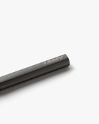 A close-up of a black LAMY Lx Rollerball (Ruthenium) pen resting on a white surface, displaying the engraved LAMY brand name on the cap. Its refillable rollerball design guarantees smooth writing with every stroke.