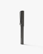 A closed black LAMY Lx Rollerball (Ruthenium) pen stands upright on a plain white background, featuring a metal clip and minimalist design—reflecting the same elegance and smooth writing experience offered by this refillable rollerball pen.