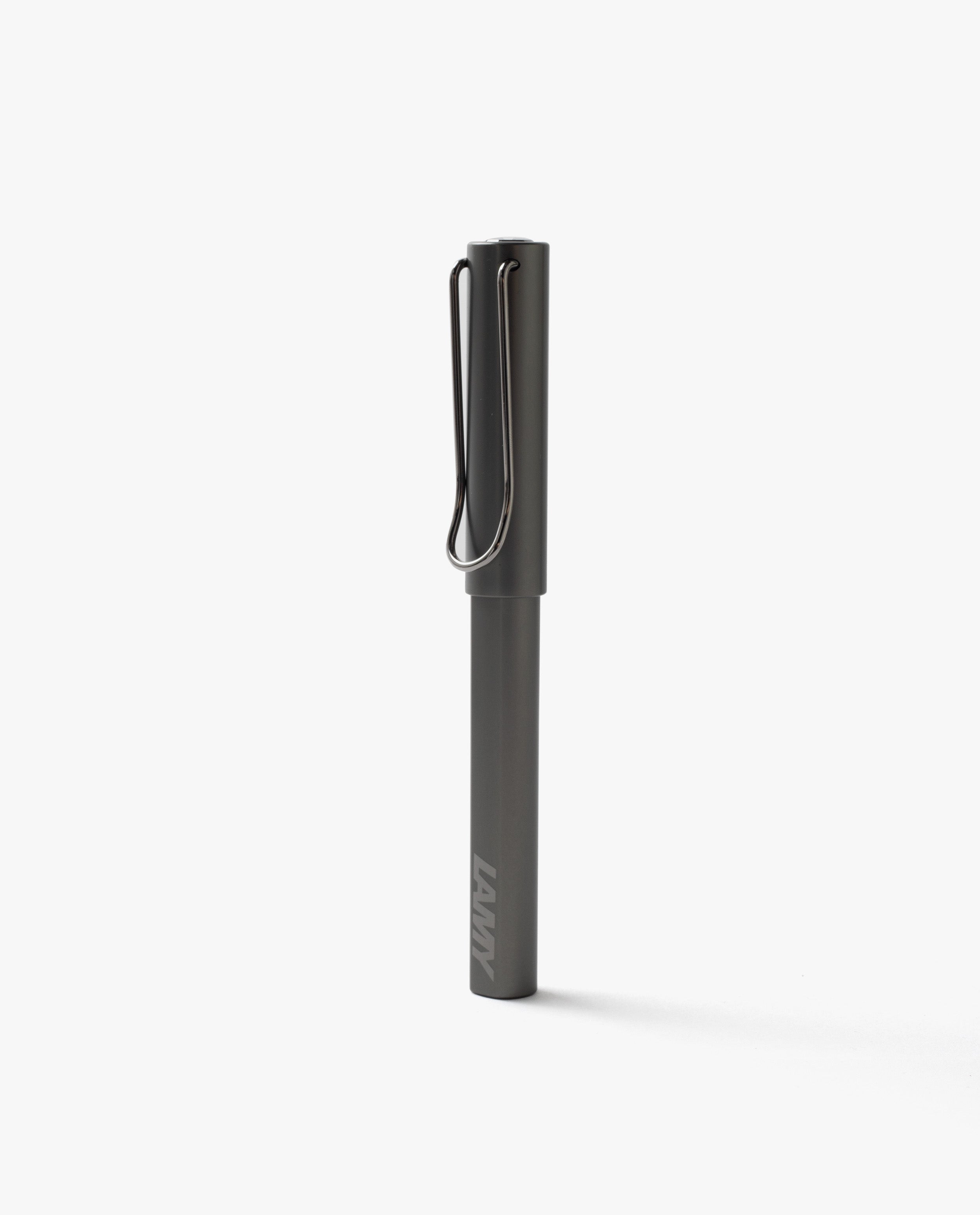 A closed black LAMY Lx Rollerball (Ruthenium) pen stands upright on a plain white background, featuring a metal clip and minimalist design—reflecting the same elegance and smooth writing experience offered by this refillable rollerball pen.