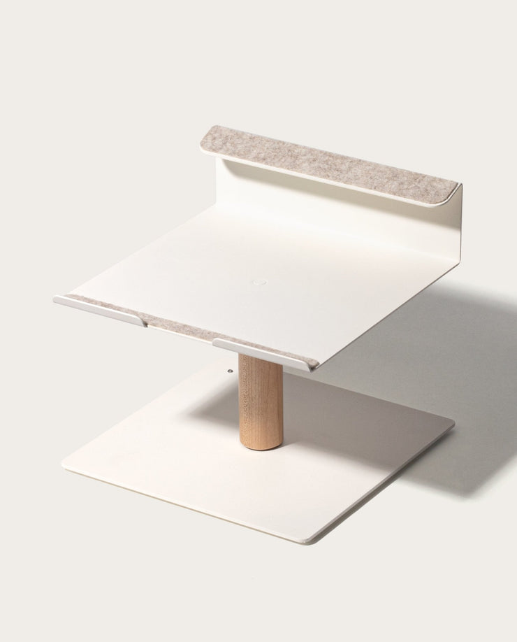 The Gather Laptop Stand (White/Maple) features a minimalist, square base and light wood central post, topped with a white square platform accented by felt padding for comfort; crafted in the USA.