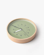 The Lemnos SOSO Clock (Green) features a round plywood design with a light wood frame and a green face. Black numbers spiral across the surface, complemented by black hour and minute hands. Resting elegantly on a white surface, this minimalist clock is an ideal addition to any modern space.