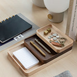 The Valet Tray Bundle (Maple - Set of 3), handcrafted in Pennsylvania, keeps pens, coins, keys, small locks, and a notepad organized on a light wood desk alongside a grey pouch, black notebook, books, and a white lamp.