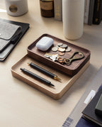 The Valet Tray (Walnut - Small), handcrafted in Pennsylvania, holds pens, keys, coins, and earbuds. Nearby sit a gray felt pouch, books, bottles, and a white tumbler on a light wood desk for everyday carry storage.