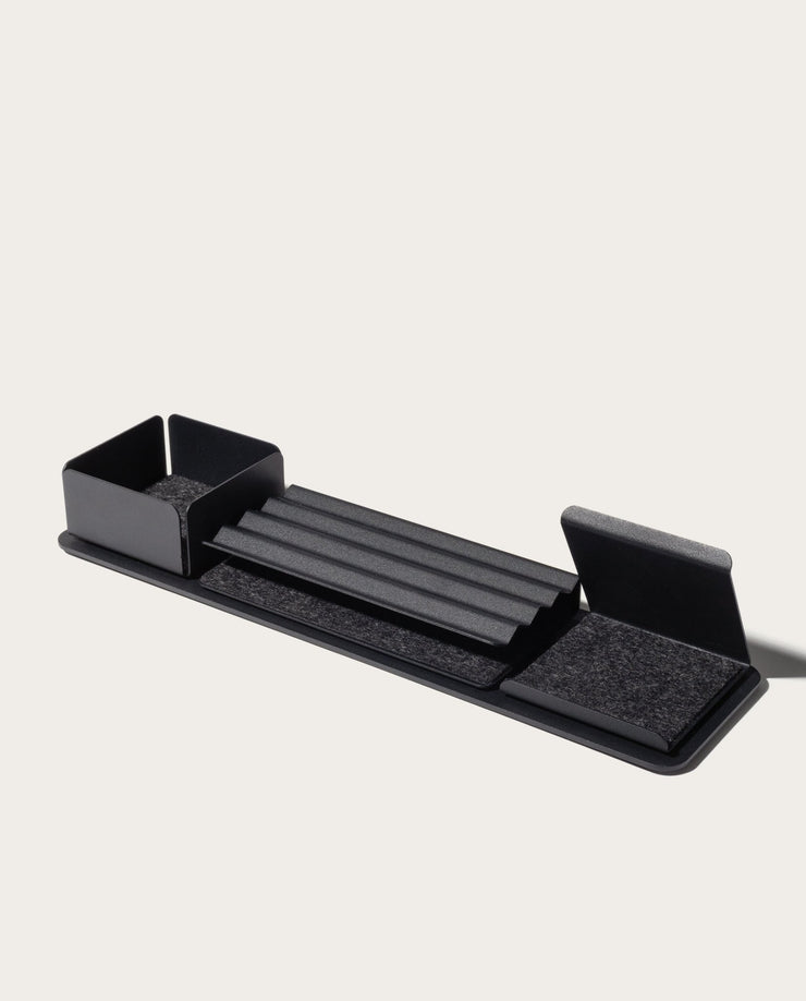 The Gather 1x4 Organizer Set (Black) is a sleek, modular desk organizer made in Pennsylvania with powder-coated steel compartments, a central grooved tray, left-side bin, and felt-lined angled sections on a rectangular base.