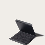 The Gather Phone Stand (1x1 - Black) is a minimalist, black, rectangular stand with a hinged lid, partially open to show its soft dark felt interior, set against a plain light background—ideal as a tablet or phone stand.