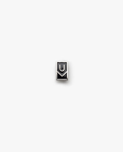 The Ugmonk Enamel Pin is a small, rectangular metallic accessory featuring a minimalist design with geometric U and M shapes on a plain white background.