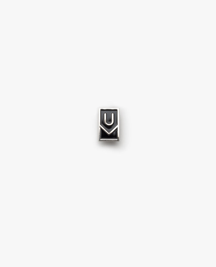 The Ugmonk Enamel Pin is a small, rectangular metallic accessory featuring a minimalist design with geometric U and M shapes on a plain white background.