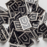 A collection of Ugmonk Enamel Pins with a geometric U-shaped design in black and silver, scattered and overlapping on a white surface.