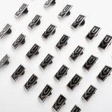 Ugmonk Enamel Pins in black rectangles and silver logos are arranged diagonally in a grid on a white background. Each pin displays a geometric U or V design.