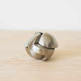 The Craighill Venn Puzzle (Stainless Steel) is displayed assembled on a light wooden surface, its smooth, curved pieces interlocking to form a striking spherical shape reminiscent of this renowned puzzle.