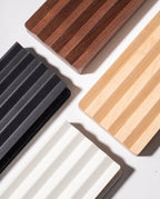 Four rectangular Gather Wood Zigzag Trays (2x1 - Walnut) with ribbed textures and varied colors are arranged diagonally on a white surface, their shadows adding dimension and highlighting the solid walnut option.